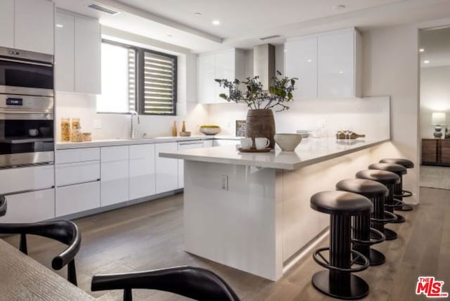 kitchen featuring double oven, white cabinetry, sink, a kitchen breakfast bar, and light hardwood / wood-style floors