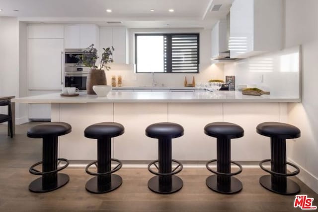 kitchen with sink, a breakfast bar area, white cabinetry, kitchen peninsula, and oven