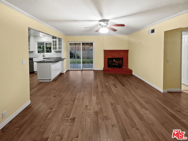 unfurnished living room featuring sink, crown molding, a brick fireplace, dark hardwood / wood-style floors, and ceiling fan