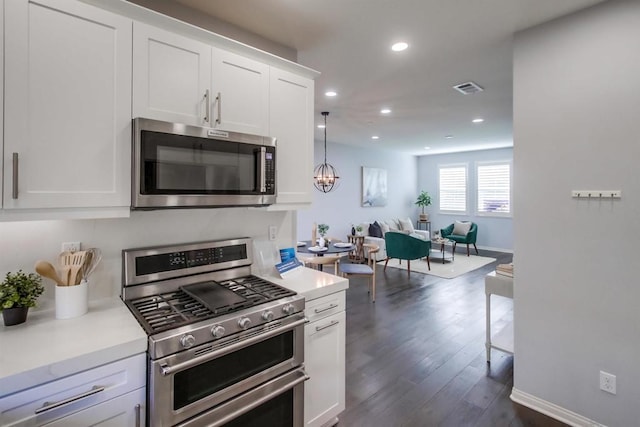 kitchen featuring pendant lighting, white cabinetry, stainless steel appliances, dark hardwood / wood-style flooring, and a chandelier