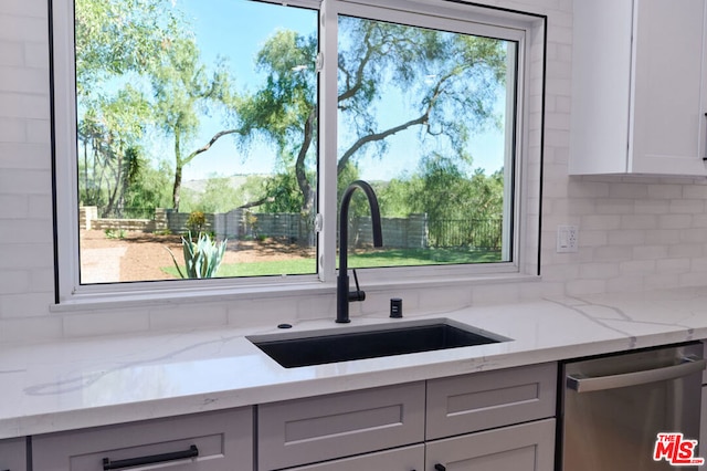 kitchen with sink, stainless steel dishwasher, gray cabinets, light stone countertops, and decorative backsplash