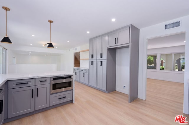 kitchen featuring pendant lighting, gray cabinets, light stone countertops, and light wood-type flooring