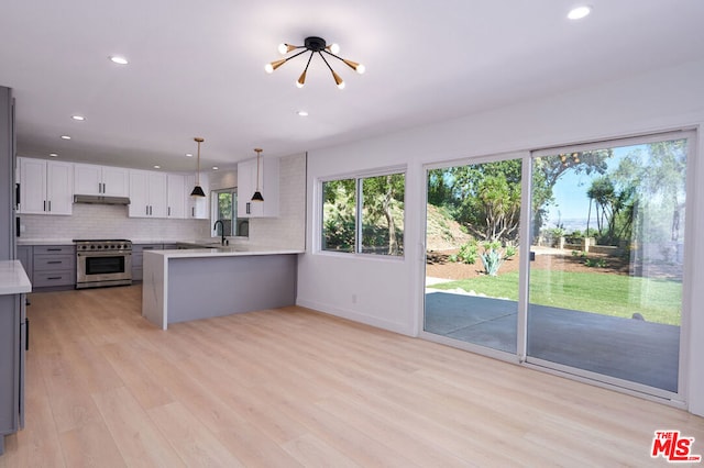 kitchen with white cabinetry, hanging light fixtures, high end stainless steel range, kitchen peninsula, and light wood-type flooring