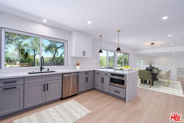 kitchen featuring sink, gray cabinetry, hanging light fixtures, stainless steel appliances, and kitchen peninsula