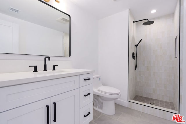 bathroom with tile patterned flooring, vanity, a tile shower, and toilet