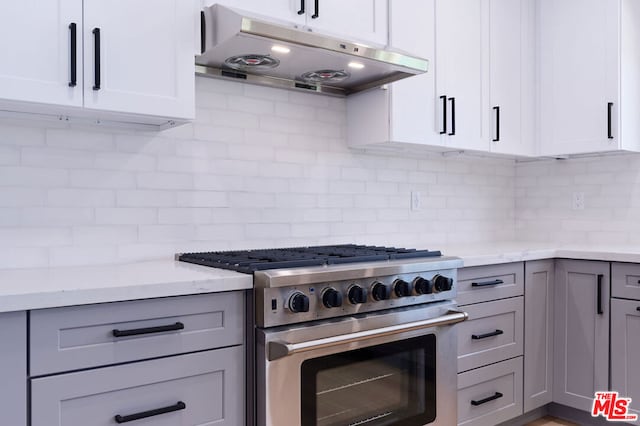 kitchen featuring high end stainless steel range oven, light stone countertops, and decorative backsplash