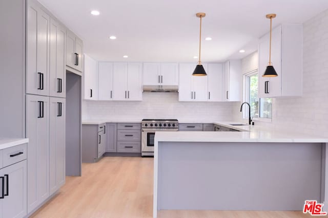 kitchen featuring tasteful backsplash, hanging light fixtures, high end stainless steel range, kitchen peninsula, and light hardwood / wood-style flooring