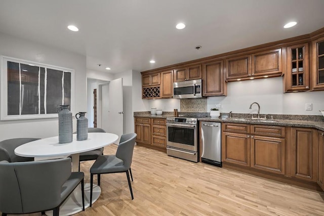 kitchen with appliances with stainless steel finishes, tasteful backsplash, sink, dark stone counters, and light hardwood / wood-style floors