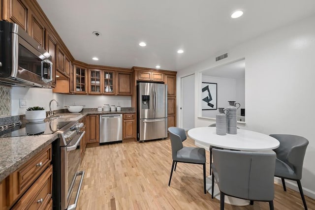 kitchen with dark stone countertops, sink, light hardwood / wood-style floors, and appliances with stainless steel finishes