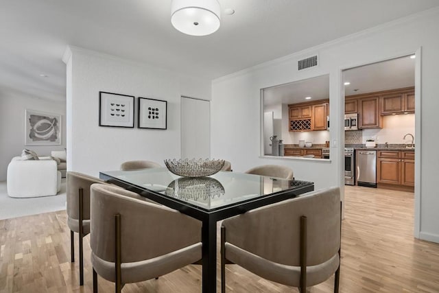 dining room with crown molding, sink, and light wood-type flooring