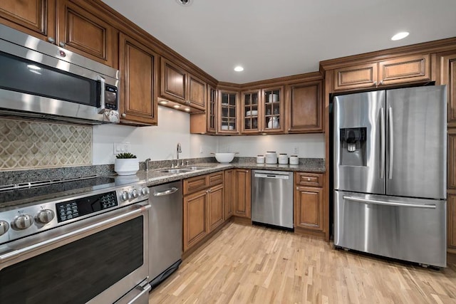 kitchen featuring sink, appliances with stainless steel finishes, light hardwood / wood-style floors, decorative backsplash, and dark stone counters