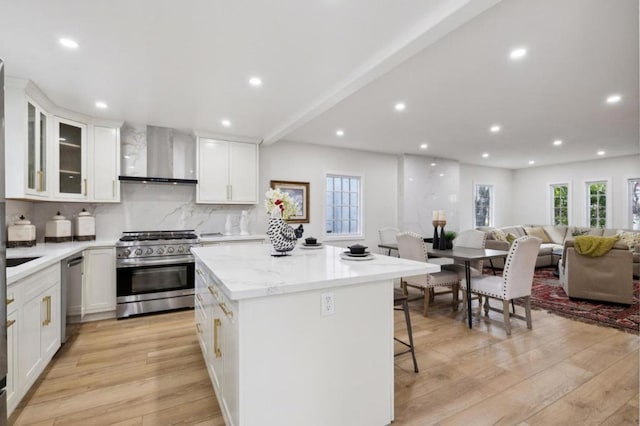 kitchen with tasteful backsplash, light hardwood / wood-style flooring, wall chimney range hood, stainless steel appliances, and white cabinets