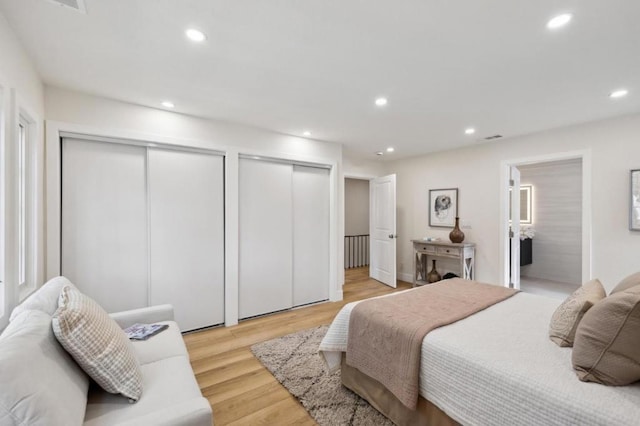 bedroom with multiple closets, connected bathroom, and light hardwood / wood-style floors