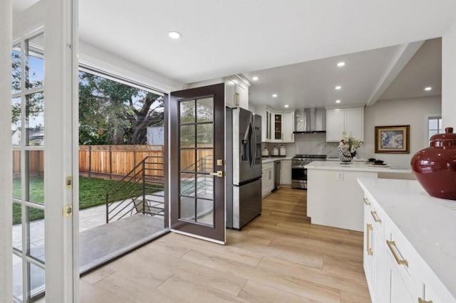 kitchen with light hardwood / wood-style flooring, appliances with stainless steel finishes, white cabinets, decorative backsplash, and wall chimney range hood