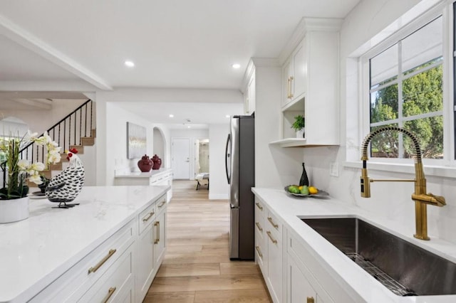 kitchen with sink, light wood-type flooring, stainless steel fridge, light stone countertops, and white cabinets