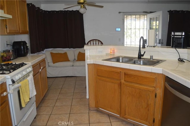 kitchen featuring sink, white range with gas cooktop, stainless steel dishwasher, tile counters, and light tile patterned floors