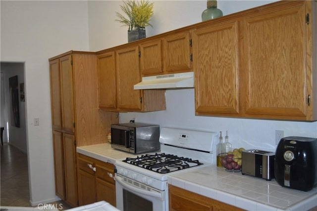 kitchen with tile patterned flooring, tile countertops, and white gas stove