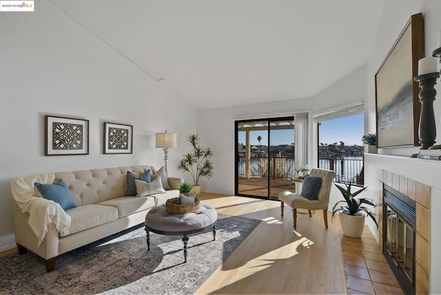 living room featuring a water view, tile patterned floors, lofted ceiling, and a fireplace