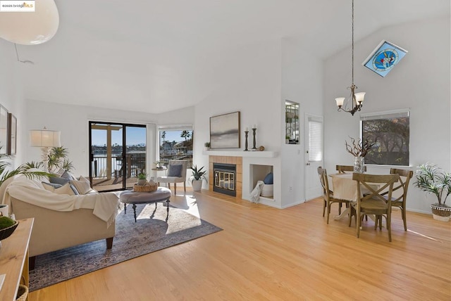 living room featuring a tiled fireplace, high vaulted ceiling, hardwood / wood-style flooring, and a chandelier