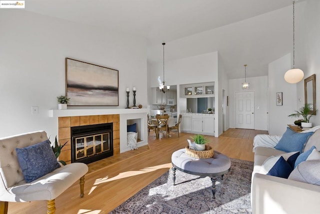 living room with a notable chandelier, a fireplace, light hardwood / wood-style floors, and high vaulted ceiling