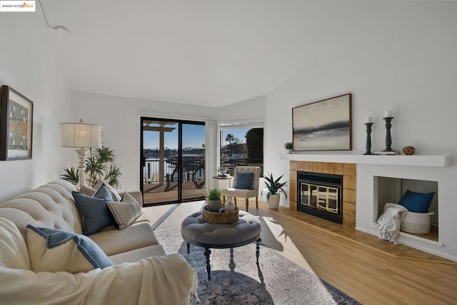 living room with a tiled fireplace, vaulted ceiling, and light hardwood / wood-style flooring