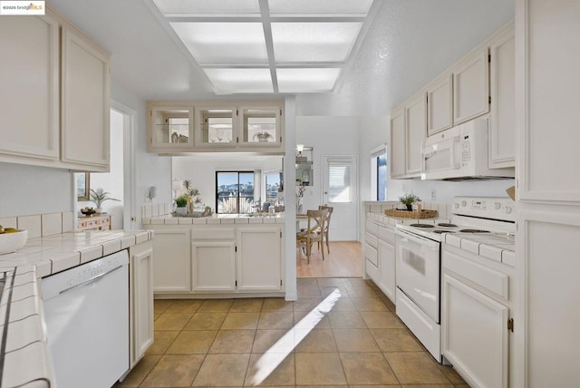 kitchen with white cabinetry, white appliances, tile counters, and light tile patterned flooring