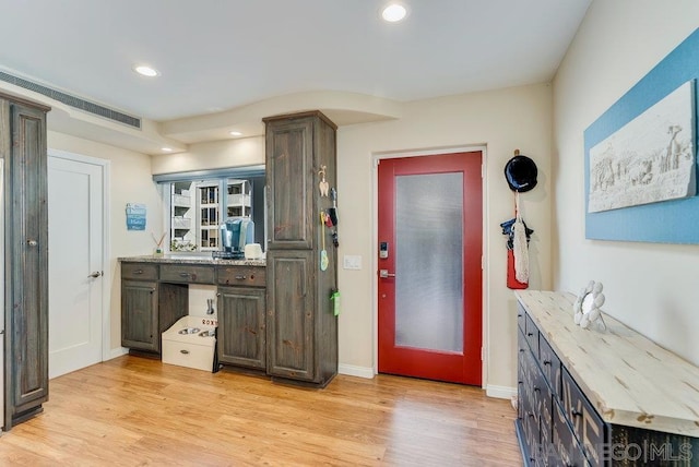 kitchen with light stone countertops, dark brown cabinetry, and light hardwood / wood-style flooring