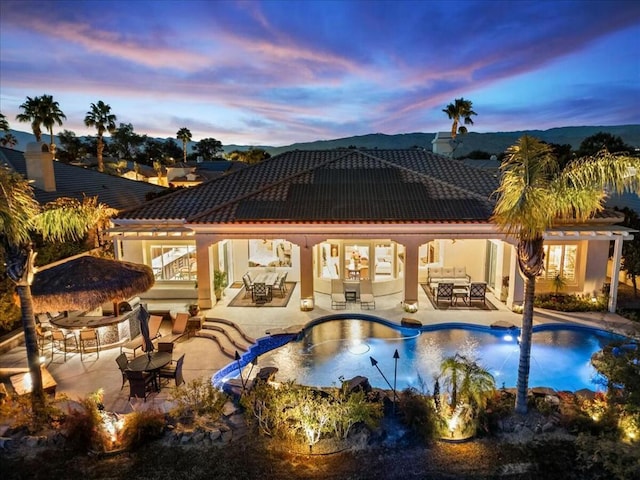 pool at dusk with a gazebo, a patio area, and a bar