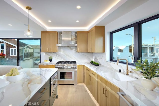 kitchen featuring appliances with stainless steel finishes, light stone countertops, wall chimney range hood, decorative light fixtures, and sink