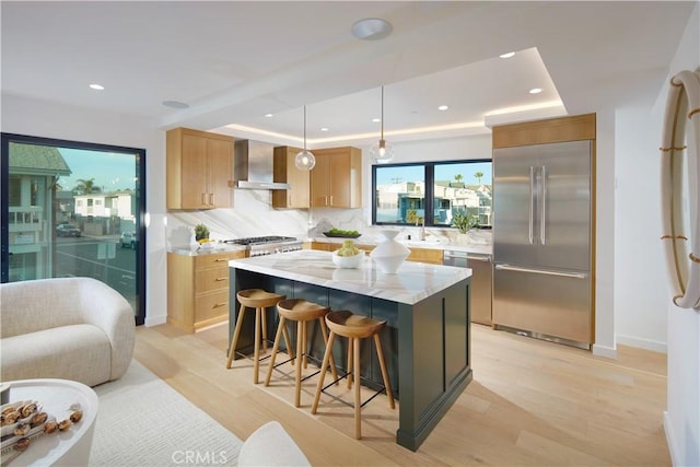 kitchen featuring a center island, light stone counters, appliances with stainless steel finishes, wall chimney exhaust hood, and pendant lighting