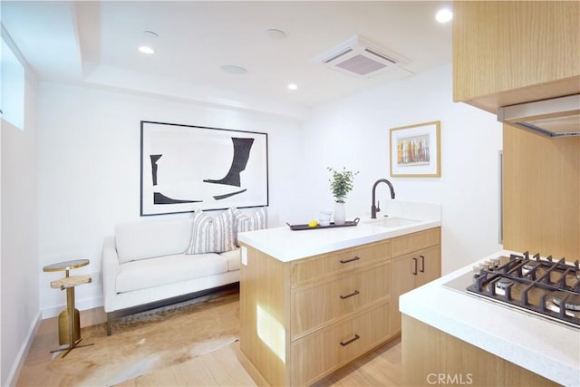 kitchen featuring sink, a center island with sink, white gas cooktop, and light brown cabinetry