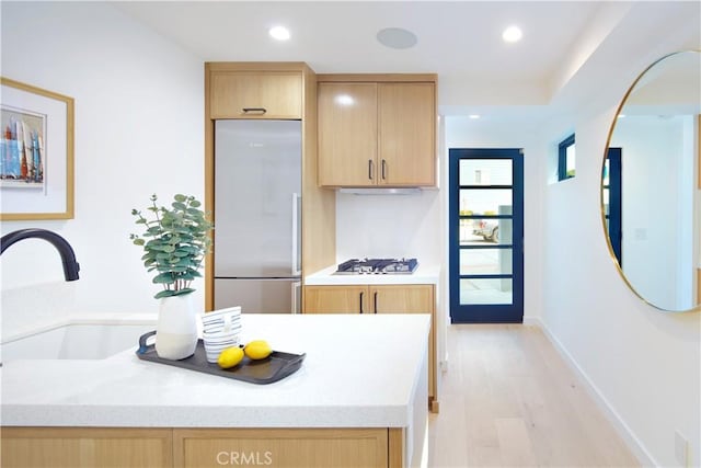 kitchen with stainless steel appliances, light hardwood / wood-style floors, ventilation hood, light brown cabinets, and sink