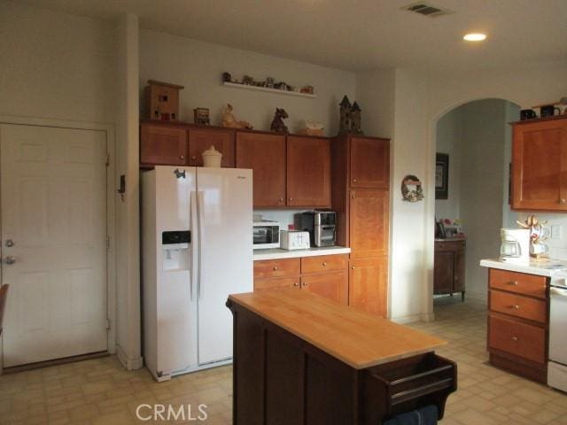 kitchen with arched walkways, light floors, visible vents, brown cabinets, and white fridge with ice dispenser