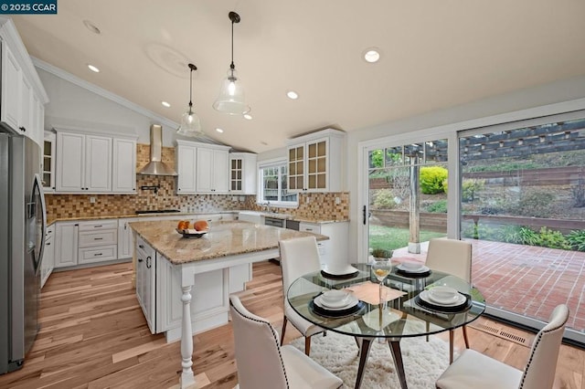 kitchen with a kitchen island, pendant lighting, white cabinets, stainless steel fridge, and wall chimney range hood