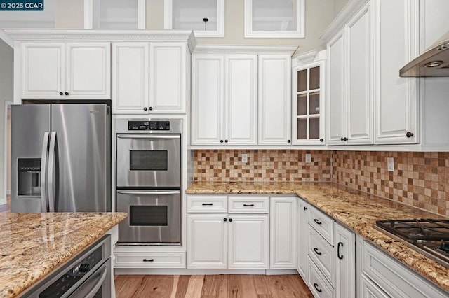 kitchen featuring stainless steel appliances, premium range hood, white cabinets, and light stone counters