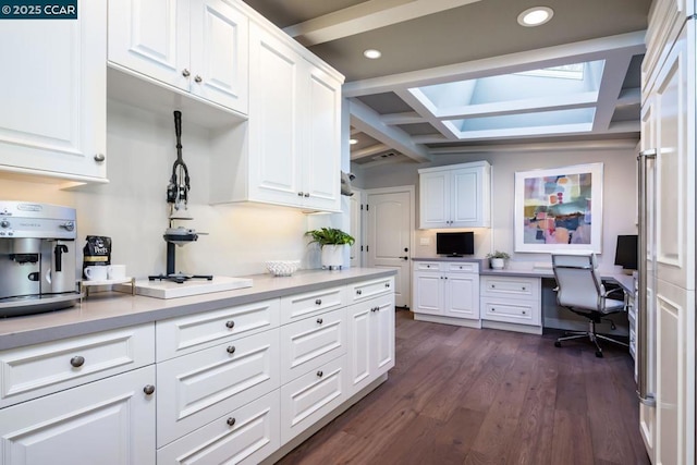 kitchen featuring dark hardwood / wood-style flooring, built in desk, lofted ceiling with skylight, and white cabinets