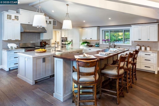 kitchen featuring white cabinetry, tasteful backsplash, lofted ceiling with beams, a kitchen breakfast bar, and an island with sink