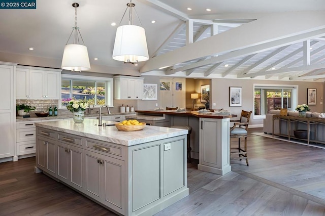 kitchen featuring sink, vaulted ceiling with beams, tasteful backsplash, pendant lighting, and a kitchen island with sink