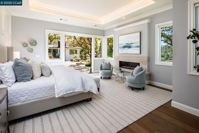 bedroom featuring hardwood / wood-style flooring, a tray ceiling, a tile fireplace, and crown molding