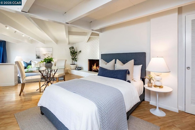 bedroom with beamed ceiling, wood-type flooring, and a brick fireplace