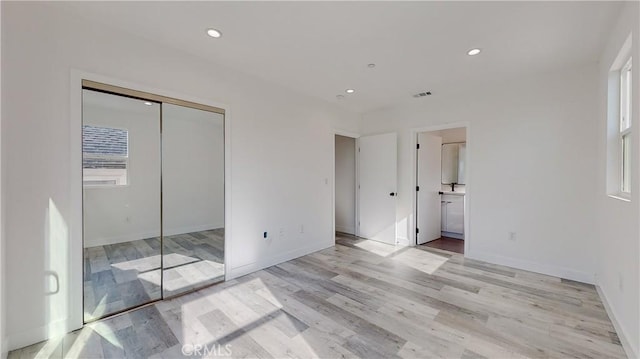 unfurnished bedroom featuring light wood-type flooring, ensuite bath, and a closet