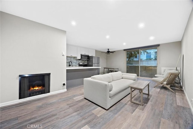 living room featuring ceiling fan, sink, and light hardwood / wood-style floors