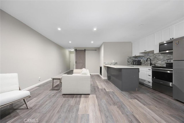 kitchen featuring white cabinetry, appliances with stainless steel finishes, a barn door, and light wood-type flooring