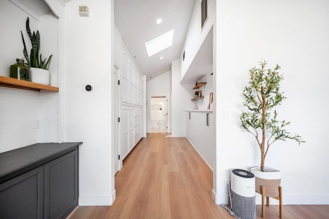 hall with lofted ceiling with skylight and light hardwood / wood-style floors