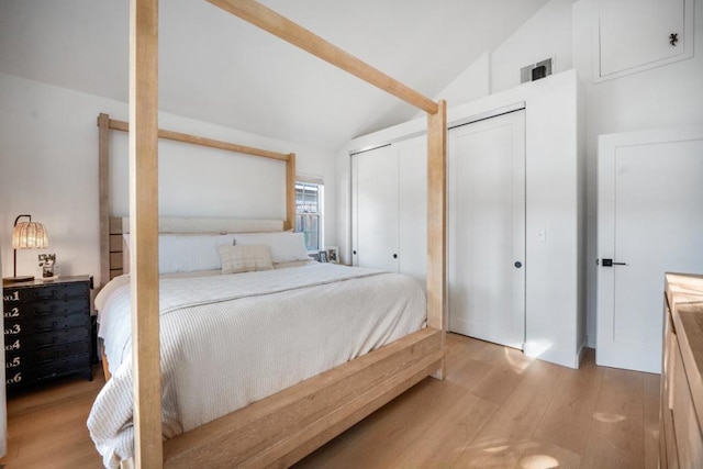 bedroom featuring multiple closets, vaulted ceiling, and light hardwood / wood-style floors