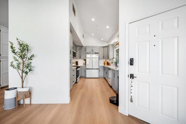 kitchen featuring stainless steel appliances, high vaulted ceiling, gray cabinets, and light hardwood / wood-style floors