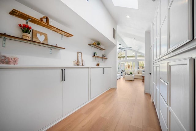 corridor with vaulted ceiling with skylight and light wood-type flooring