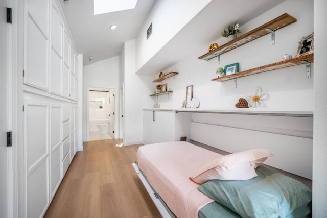 bedroom featuring connected bathroom, lofted ceiling with skylight, and light hardwood / wood-style floors