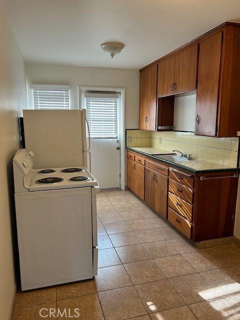 kitchen with sink, tasteful backsplash, light tile patterned floors, fridge, and electric range