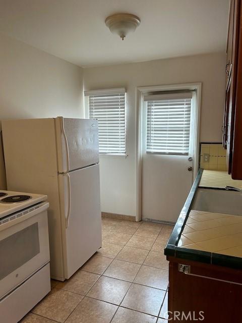 kitchen with light tile patterned flooring, sink, tile counters, and white appliances